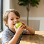 Child biting into a green apple, illustrating food consistency and its role in craniofacial development