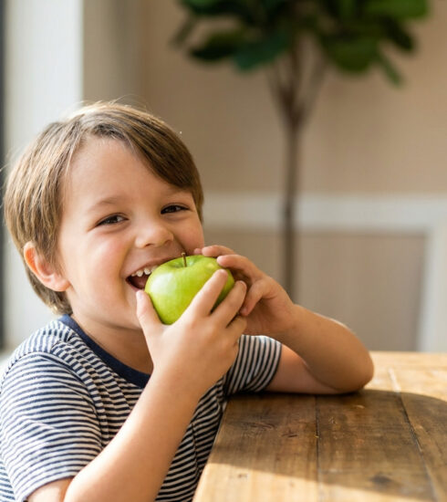 Child biting into a green apple, illustrating food consistency and its role in craniofacial development