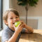 Child biting into a green apple, illustrating food consistency and its role in craniofacial development